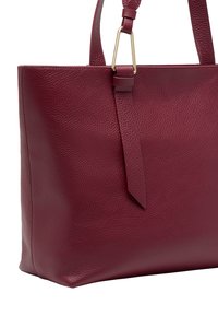 Borsa tote in pelle bordeaux con superficie texturizzata, fondo piatto e una lunga tracolla con un dettaglio in metallo color oro.