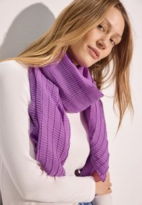 Scaldino pieghettato viola con una texture morbida, che si appoggia elegantemente. Tessuto leggero con un motivo a onde e bordi grezzi, disposto a strati attorno al collo.