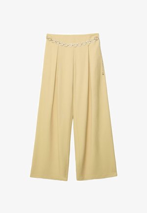 Beige broek met wijde pijpen en plooien, met een zilverkleurige kettingriem met ronde schakels die schuin over de tailleband hangt.