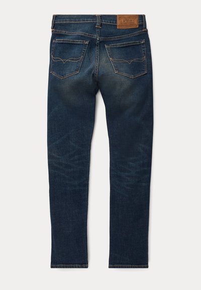 Jeans de denim azul escuro com um corte slim, apresentando um patch de couro na cintura e duas bolsas traseiras com detalhes em costura.