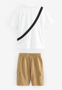 Camiseta blanca con una franja diagonal negra, combinada con pantalones cortos beige que cuentan con dos bolsillos laterales y una cinturilla elástica.