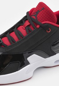 Schwarze und rote Sneakers mit einem strukturierten Mesh-Obermaterial, glänzenden Lackleder-Akzenten und einer weißen Zwischensohle. Mit schwarzen Schnürsenkeln und einer roten Zunge.