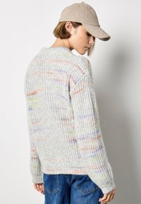 Maglione grigio chiaro a maglia testurizzata con righe multicolori. Presenta un collo a giro e polsini a costine, abbinato a un berretto beige e jeans blu.