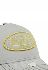Halli halli kübar hall, millel on tikitud kuldne ovaalne logo tekstiga "Von Dutch" ja "ORIGINALS". Näha on kulumist ja kulunud tekstuuri äärel.