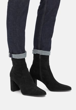 Stivaletti in camoscio nero con punta appuntita e tacco alto cilindrico. Caratterizzati da una cerniera laterale e una texture liscia. Jeans in denim con orli risvoltati.