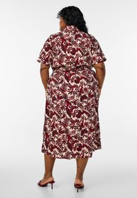 Vestido midi con estampado floral en beige y rojo profundo, mangas cortas, tejido suave, cintura ceñida, con grandes patrones de hojas y flores.