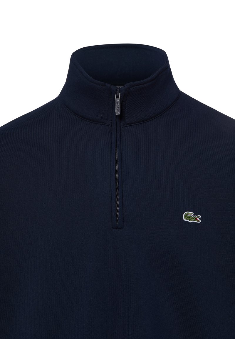 Maglione blu navy con zip a quattro e piccolo logo verde coccodrillo sul lato sinistro del petto.