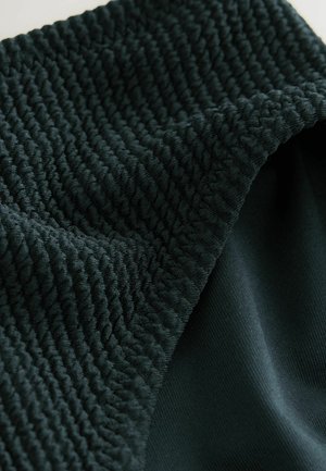 Tume roheline kangas, millel on tekstureeritud ribakujuline muster ja siledad osad. Materjal näeb välja pehme ja veniv, nähtavate õmblustega.