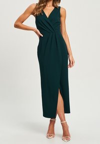 Vestido midi sin mangas de color verde oscuro con un diseño envolvente, que presenta una abertura frontal y pliegues verticales. Textura suave y silueta elegante.