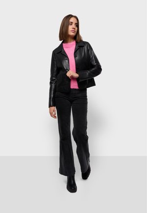 Veste en cuir noir courte, pull rose pelucheux, jean noir évasé et bottes noires à la cheville. Texture lisse, fermeture à boutons sur la veste.