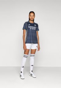 Navy soccer jersey with white and green accents, paired with white shorts and knee-high white socks featuring black stripes. Sports shoes included.