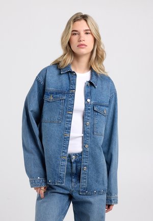 Spijkerjasje in middelblauw, met een relaxte pasvorm, knoopsluiting aan de voorkant, twee borstzakken en zilveren accenten op de manchetten en zoom.