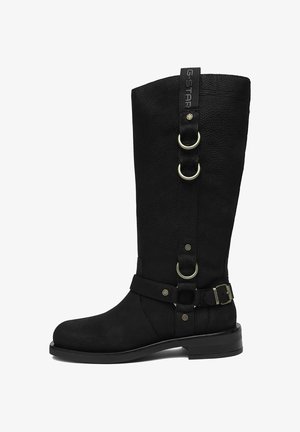 Bota negra de cuero hasta la mitad de la pantorrilla con aros plateados y detalles de correa con hebilla, suela plana y marca G-Star en la lengüeta superior.