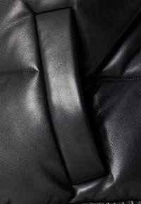 Zbliżenie na czarną skórzaną teksturę z wyściełanym pionowym paskiem i subtelnymi detalami przeszycia na miękkiej powierzchni.