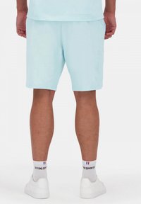 Pantalones cortos deportivos de color azul claro, fabricados con un tejido transpirable, con una cinturilla elástica y bolsillos laterales. Se pueden ver zapatos blancos y calcetas con logotipo.