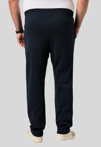 Marina blå mjukisbyxor i mjukt tyg med elastisk midja, avsmalnande ben och en bakficka. Kombinerade med ljusa sneakers.