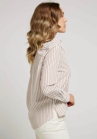 Chemise à rayures blanche et marron, avec un col, des manches longues et un ourlet légèrement arrondi avec des fentes sur les côtés.