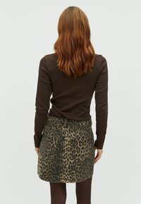 Un top bronz cu maneci lungi, asortat cu o fustă din denim cu imprimeu leopard, având talie înaltă, două buzunare la spate și un croi drept.