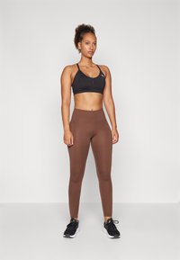 Soutien-gorge de sport noir et leggings marron taille haute en matériau extensible, associés à des chaussures de sport noires pour un look fitness.