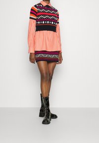 Värikäs neulepaita, jossa oransseja, mustia ja vaaleanpunaisia kuvioituja raitoja, vaaleanpunaraidallisen paidan päällä; yhdistetty mustiin kiiltäviin nilkkureihin.