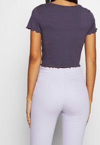 Skuren, mörkgrå t-shirt med vågiga ärmar, ihop med högmidjade lavendelfärgade byxor. Tyget verkar mjukt och lätt.