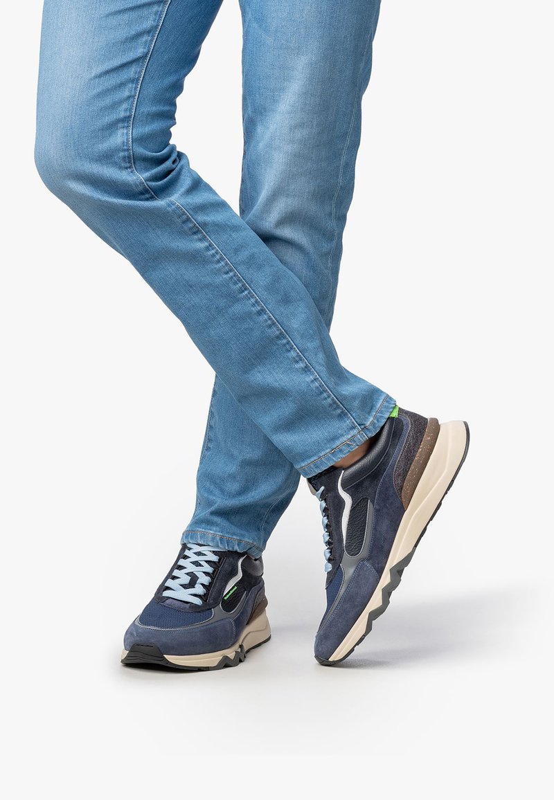 Modré sportovní boty s texturovanou tkaninou, prvky z jemné síťoviny a kontrastní bílou podrážkou. Spárovány se světle modrými džíny.
