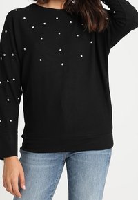 Svart långärmad tröja med avslappnad passform, prydd med spridda silverdetaljer, rund halsringning samt ribbade muddar och nederkant.