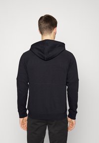 Sweatshirt noir à capuche en tissu doux, avec manches raglan, coupe décontractée et coutures visibles le long des jointures.