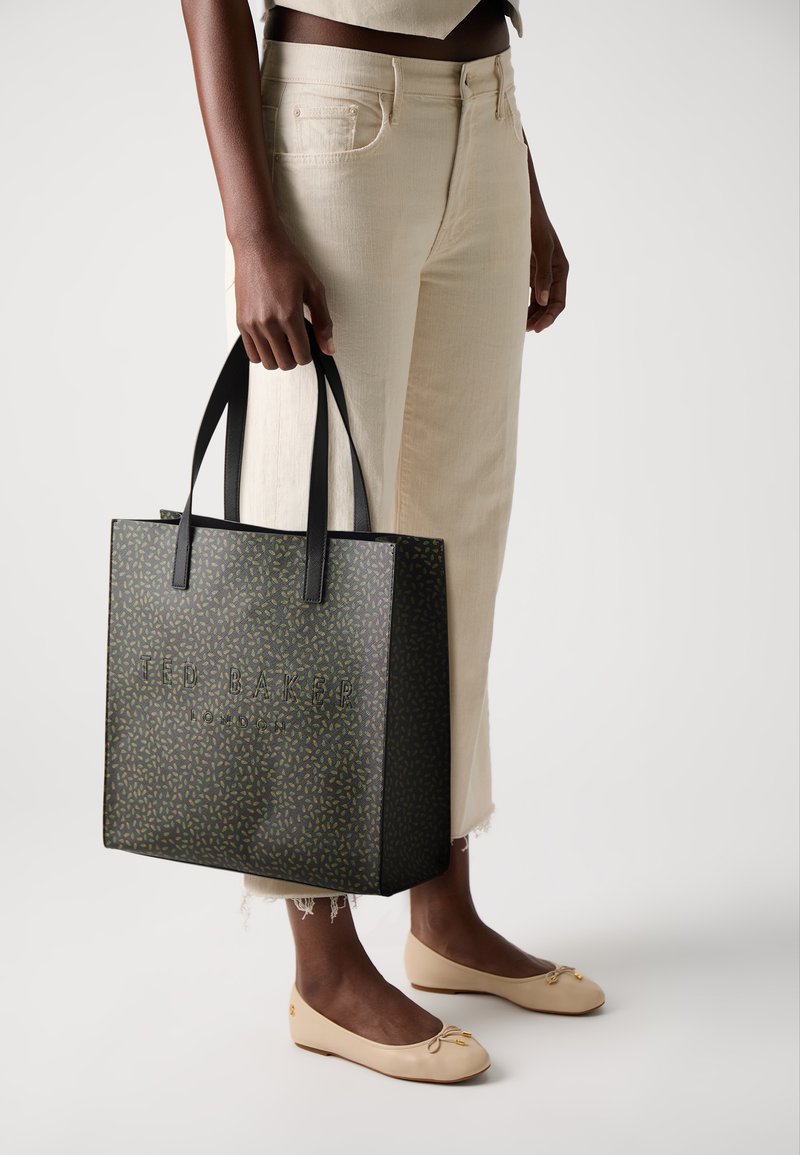 Toteveske i mørkegrønn med gullbladmønster, med preget tekst "Ted Baker", robuste svarte håndtak og strukturert kvadratisk design.