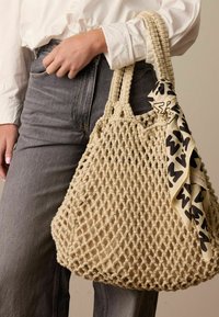 Natuurlijke geweven tote bag met een netpatroon, in een crèmekleur. Inclusief een met een patroon van zwart en crème sjaal die aan de handgreep is geknoopt.