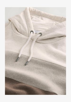 Sudadera con capucha beige con diseño de bloques de color que incluye secciones en marrón claro y topo. Cuerda ajustable y detalles en hardware metálico.