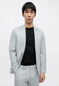 Világosszürke öltöny finom kockás mintával, fekete pólóval alatta, karcsúsított szabás, egysoros, egygombos zakó oldalzsebekkel.