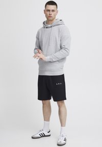 Sweat à capuche gris avec cordons, shorts noirs avec le texte blanc "A.R.C.", et chaussures de sport rayées gris/noir.