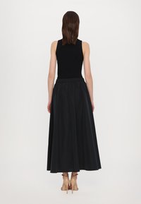 Sort ribbet tank topp kombinert med et langt, flytende svart skjørt. Stoffet har en jevn tekstur, med en samlet midje.
