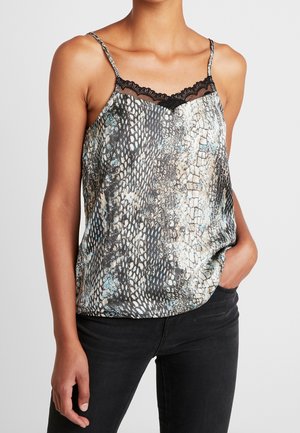 Kobieta ubrana w bezrękawnik z wzorem w skórę węża z czarną koronkową lamówką, w połączeniu z czarnymi spodniami, z ręką w kieszeni.