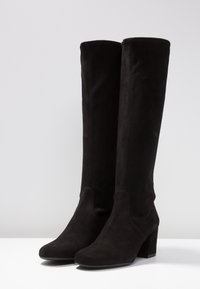 Bottes noires en suede, arrivant juste au genou, avec un design épuré, un bout arrondi et un talon carré de 3 pouces ; dotées d'une texture lisse et de peu de détails.
