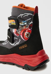 Μαύρο και γκρι μποτάκι μέχρι τον αστράγαλο με πορτοκαλί εσωτερικό, διακοσμημένο με γραφικό ενός τέρας φορτηγού, λουράκι Velcro και κόκκινη σόλα με υφή.