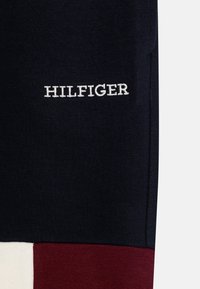 Marineblauwe katoenen kleding met rode en crèmekleurige kleurvlakken. Voorzien van een geborduurd "HILFIGER"-logo in het wit op het marineblauwe gedeelte. Zachte textuur.