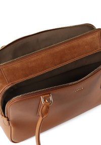 Καφέ δερμάτινη τσάντα με απαλή υφή, που διαθέτει φερμουάρ σε χρυσό τόνο και εσωτερικές τσέπες. Το όνομα της μάρκας "Furla" είναι ανάγλυφο στην επιφάνεια.