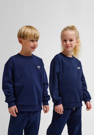 Navyblauwe sweaters met ronde hals, lange mouwen en geribde manchetten; beide hebben een klein logo op de borst. Zachte stof met een gladde textuur.