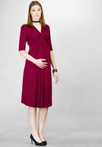 Sukienka ciążowa w ciemnym burgundzie; midi z dopasowanym topem, krótkimi rękawami i marszczonym detalem w pasie, zestawiona z czarnymi szpilkami.