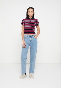 Polokošeľa s červenými a námorníckymi pásmi, golierom, v kombinácii so svetlomodrými džínsami rovného strihu a béžovými teniskami. Jednoduchý dizajn, ležérny strih.