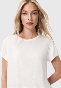 T-shirt bianco a maniche corte con una consistenza morbida e leggera, dotato di scollatura rotonda e risvolti. Design semplice e minimalista.