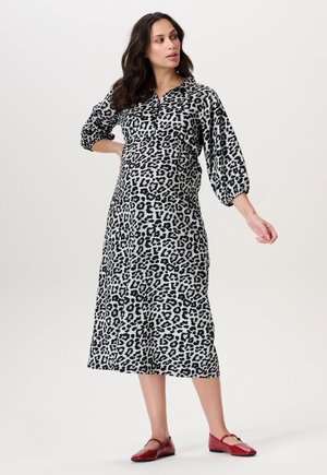 Leopardprint, lange mouwen, knoop jurk van zwart-wit stof met een relaxte pasvorm. Gekleed met rode flats, die een gladde textuur tonen.