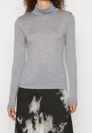Femme portant un haut à col roulé gris clair ajusté à manches longues et une jupe noire avec des motifs abstraits blancs.