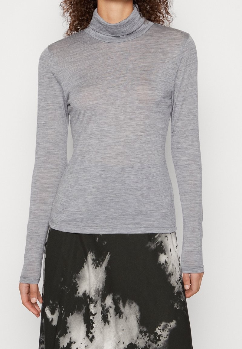 Femme portant un haut à col roulé gris clair ajusté à manches longues et une jupe noire avec des motifs abstraits blancs.