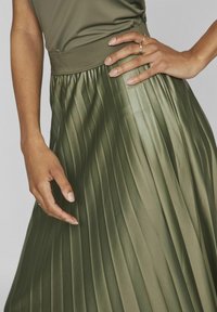 Falda plisada de color verde oliva con un acabado texturizado, que presenta una amplia cinturilla elástica y un patrón de pliegues horizontales, acentuada por una colocación a mano.