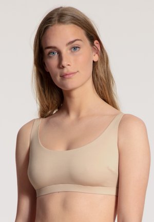 Beige draadloze bh met brede banden, een gladde textuur en een ronde halslijn. Heeft een naadloos ontwerp en een zachte, comfortabele band.