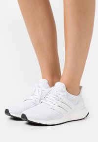 Vita mesh löparskor har ett strukturerat övre, tre sidostripes, snörning och en boost-sula med en svart gummisula.