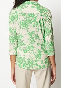 Blommönstrad topp med trekvartsärmar, med en ljuskrämfärgad bakgrund och livfulla gröna lövmönster. Mjuk tygkvalitet, avslappnad passform.